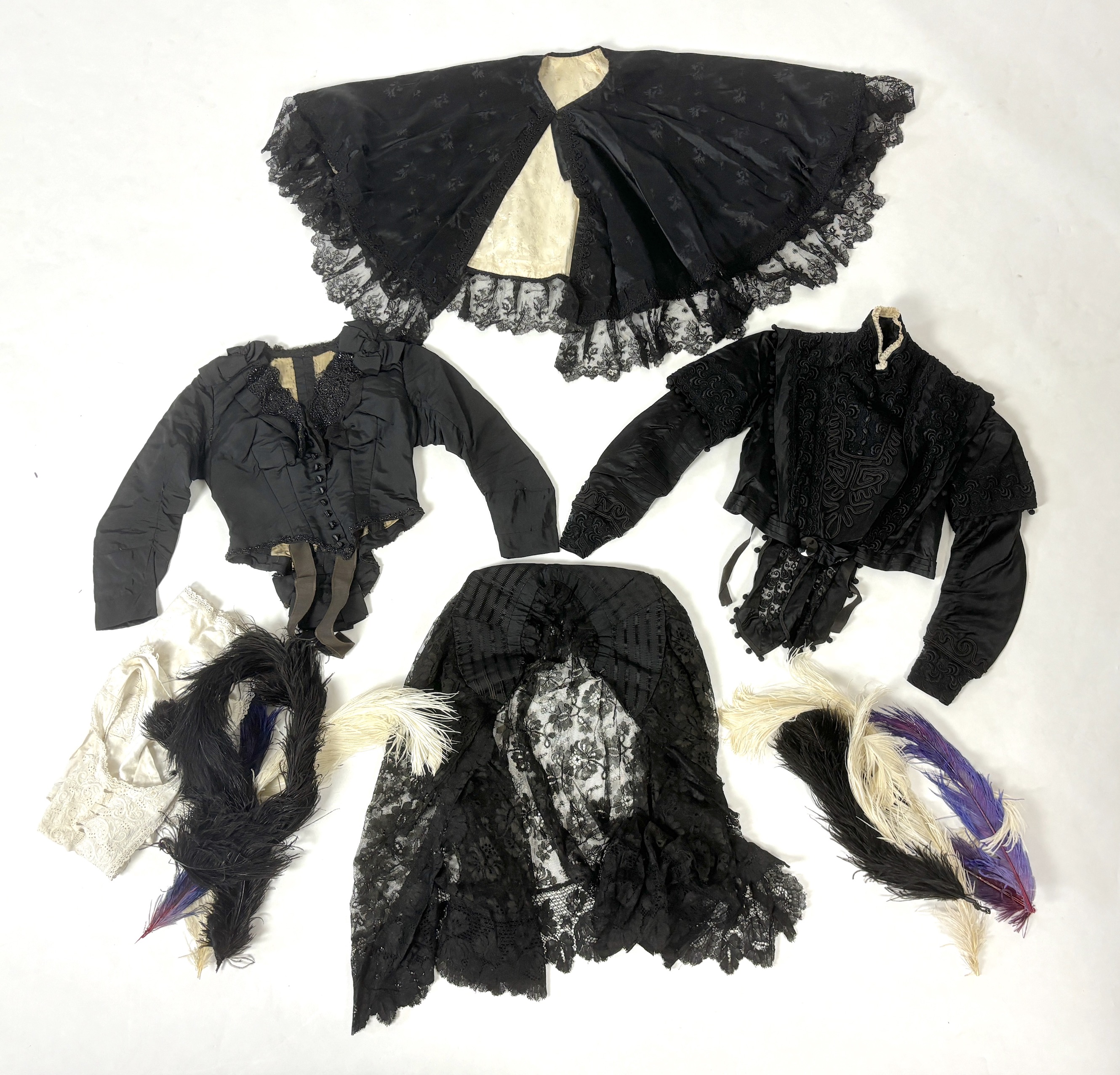 Two ladies Victorian black satin and lace, bead trimmed bodices, together with a black lace cape, a black satin cape, a small collection of coloured feathers and a child’s white worked pinafore